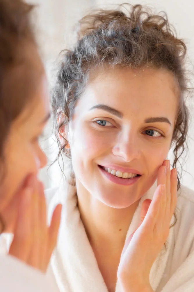 woman-applying-cream-face-while-looking-mirror